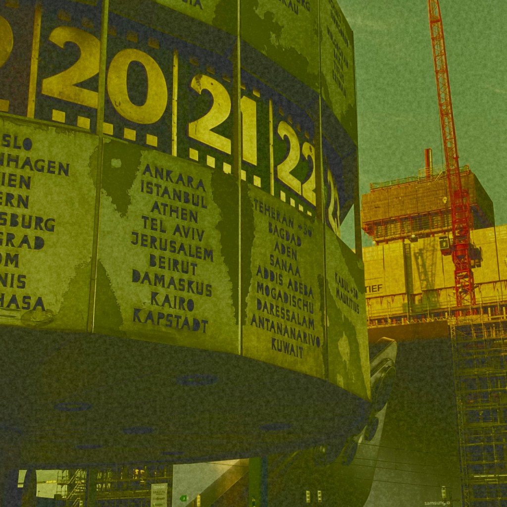The World Clock sculpture at Alexanderplatz Berlin is seen from the side showing near Asia. An enormous mobile phone advertisement lurks behind it.